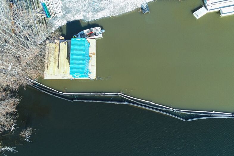 Flygbild över en sjö där oljeläns och avspärrningsläns lagts ut.