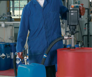 En person som använder en ATEX pump för att pumpa vätska från ett plåtfat till en plastdunk.