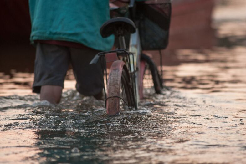 Person som leder en cykel vid översvämning.