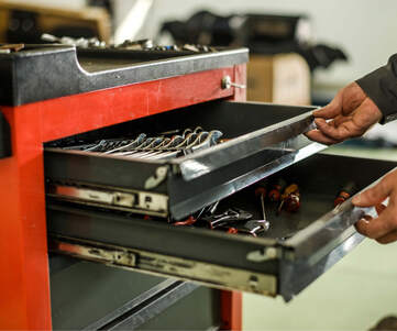 Händer som drar ut två lådor på en röd verktygsvagn fylld med verktyg.