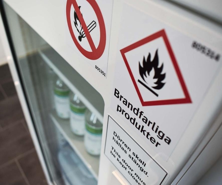 Brandskåp med glasdörr och märkning med farosymbol brandfarliga produkter.
