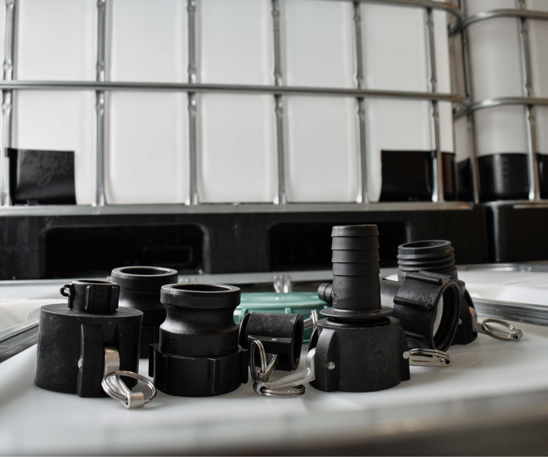 Adaptrar med kamlock-koppling och slangkoppling som ligger på en IBC tank. I bakgrunden syns flera IBC.