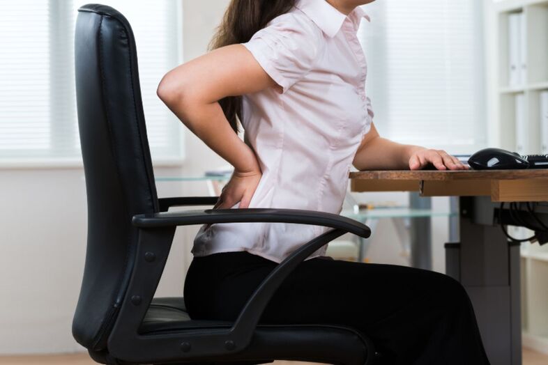Person som sitter på en kontorsstol och tar sig på ryggen. 