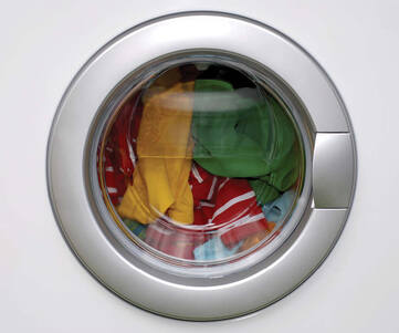 Fönstret på en tvättmaskin fylld med färgglada kläder som tvättas.